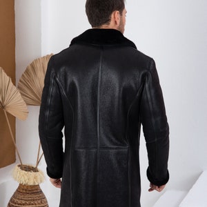 Puede incluir: Una chaqueta de cuero negro con cuello y pu&ntilde;os de piel de oveja. La chaqueta es larga y tiene un dise&ntilde;o cl&aacute;sico.