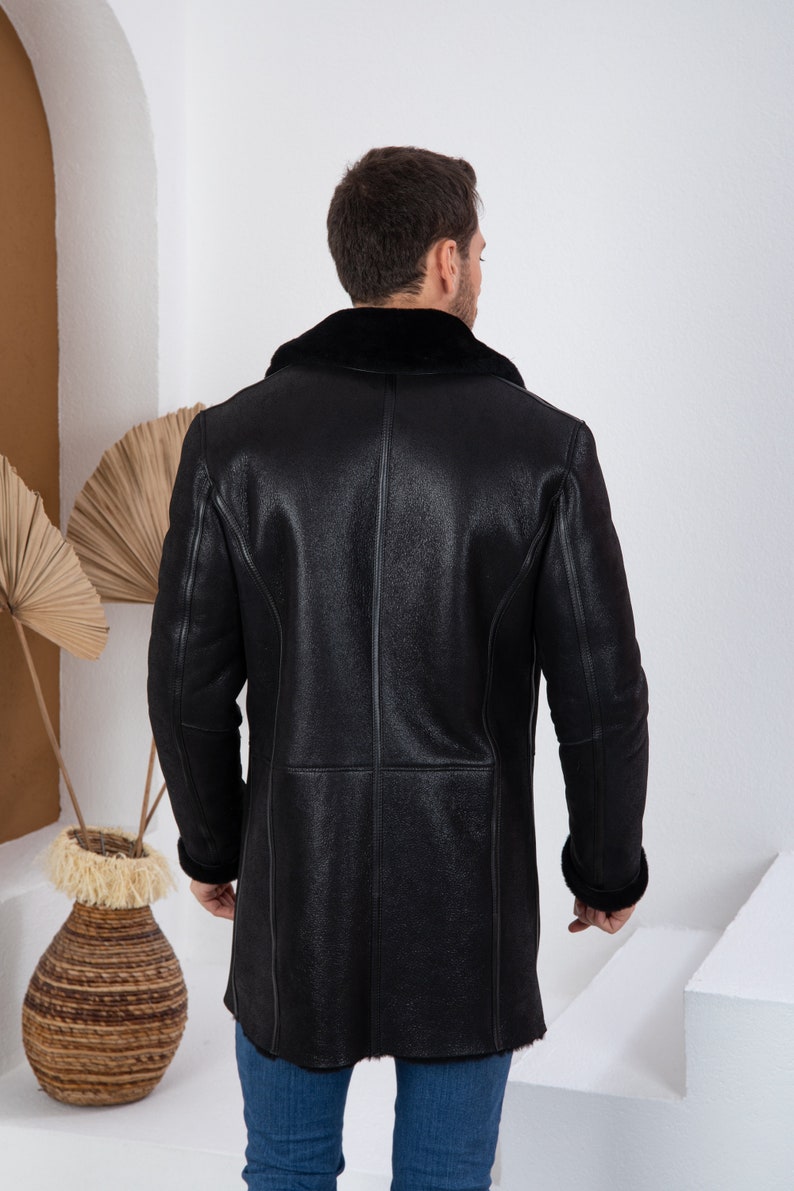 Puede incluir: Una chaqueta de cuero negro con cuello y pu&ntilde;os de piel de oveja. La chaqueta es larga y tiene un dise&ntilde;o cl&aacute;sico.