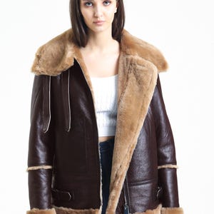 May include: A brown leather jacket with a shearling collar and lining. The jacket features a zip closure, side pockets, and shearling trim on the cuffs and hem. The jacket is a classic style, suitable for cold weather.