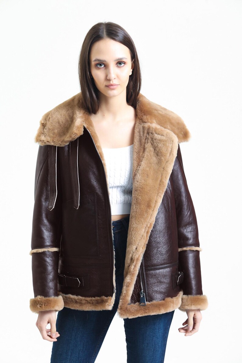 May include: A brown leather jacket with a shearling collar and lining. The jacket features a zip closure, side pockets, and shearling trim on the cuffs and hem. The jacket is a classic style, suitable for cold weather.