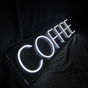 May include: White neon sign with the word "COFFEE" in a black frame.