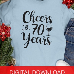 May include: A light blue t-shirt with the text "Cheers to 70 years" in black lettering and a wine glass graphic.