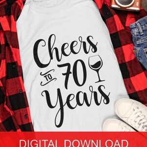 May include: White t-shirt with black text that reads "Cheers to 70 Years" and a black silhouette of a wine glass.