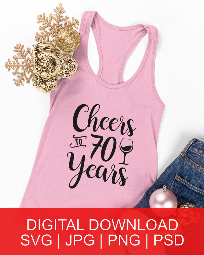 May include: Pink tank top with black text that reads "Cheers to 70 Years" with a wine glass graphic. The tank top is laying on a white surface with gold and pink ornaments.