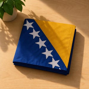 Op de afbeelding: Een gevouwen stoffen vlag met een blauw veld, een diagonale gele streep en een rij van zeven witte vijfpuntige sterren. Het ontwerp is zo georiënteerd dat het gele gedeelte zich aan de rechterkant bevindt en het blauwe gedeelte aan de linkerkant.