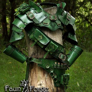 Può includere: Set di armature in pelle verde con dettagli intricati, tra cui spallacci, corazza e cintura con tasche e fiale. L'armatura è esposta su un tronco d'albero, con il logo "Faun Forge".