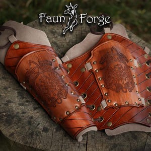 May include: A pair of brown leather arm guards with intricate Celtic knotwork designs. The arm guards are secured with rivets and lacing, and feature the text "Faun Forge" in a stylized font.