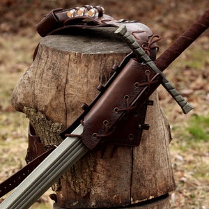 May include: A brown leather sword scabbard with a metal sword strapped to a tree stump. The scabbard has a decorative lace pattern and is secured with a metal buckle.