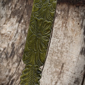 May include: A green leather strap with a floral design embossed into the surface. The strap is narrow and has a pointed end.