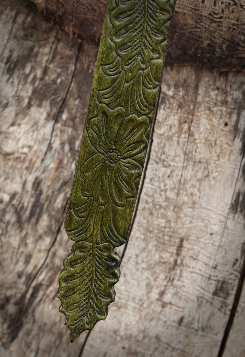 May include: A green leather strap with a floral design embossed into the surface. The strap is narrow and has a pointed end.