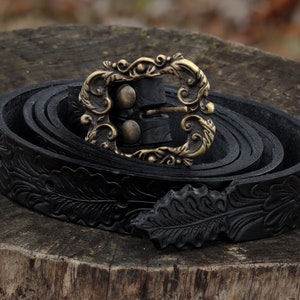 May include: A black leather belt with an ornate gold buckle and a floral design. The belt is rolled up and the buckle is closed.