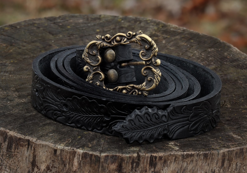 May include: A black leather belt with an ornate gold buckle and a floral design. The belt is rolled up and the buckle is closed.