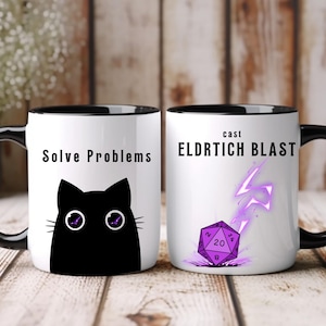 Puede incluir: Dos tazas de cerámica blancas con asas y bordes negros. Una taza presenta un gráfico de gato negro con el texto "Solve Problems". La otra taza tiene un gráfico de dados morados con el texto "cast ELDRTICH BLAST".