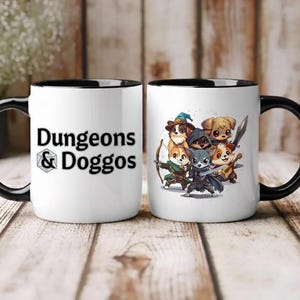 May include: Two white ceramic mugs with black handles and rims. One mug features the text "Dungeons & Doggos" in black. The other mug displays a group of cartoon dogs dressed as fantasy characters. The mugs are on a wooden surface.