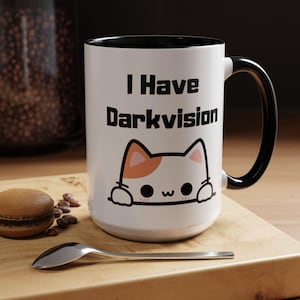 May include: White ceramic mug with a black rim and handle. The mug has a black and white illustration of a cat with orange ears peeking over the top of the mug. The text "I Have Darkvision" is printed in black on the mug.