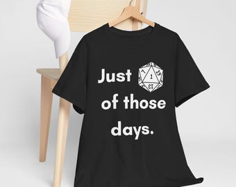 May include: Black t-shirt with white text that reads "Just one of those days." and a white graphic of a twenty-sided die.