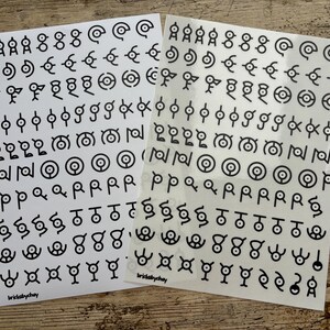 May include: Two sheets of white sticker paper with black symbols. The symbols are various shapes and designs, including circles, squares, and triangles. The text "brickabychay" is printed on each sheet.