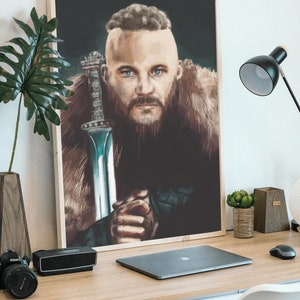 May include: A framed poster of a man with a beard and a shaved head, holding a sword. He is wearing a fur-lined coat and has a serious expression on his face. The background is dark.