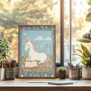 May include: A framed print featuring a white unicorn with a pink mane and tail, reading a book in a field of flowers under a blue sky with clouds. The print is labeled "FOLK AND FOREST ART".