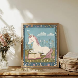 May include: A framed print featuring a white unicorn with a pink mane and tail, reading a book in a field of flowers. The artwork has a blue background with clouds and is framed in a wooden frame. The text "FOLK AND FOREST ART" is at the bottom.