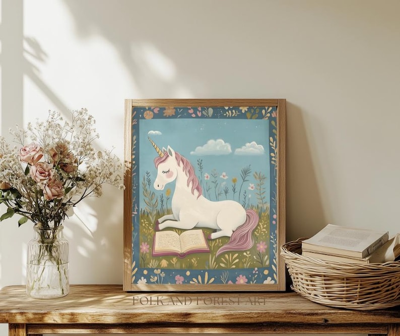 May include: A framed print featuring a white unicorn with a pink mane and tail, reading a book in a field of flowers. The artwork has a blue background with clouds and is framed in a wooden frame. The text "FOLK AND FOREST ART" is at the bottom.