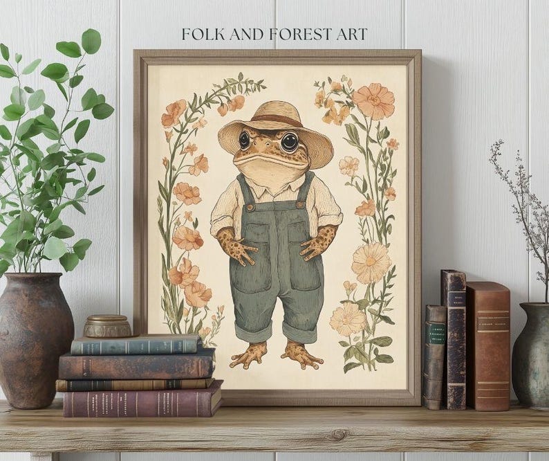 May include: A whimsical illustration of a frog wearing overalls and a straw hat, surrounded by delicate flowers in shades of pink and yellow. The artwork is framed in a light brown wood frame and features the text "Folk and Forest Art".