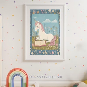 May include: A framed art print featuring a white unicorn with a pink mane and tail, reading a book in a field of flowers. The artwork is set against a blue sky with clouds, framed in a white border. The text "FOLK AND FOREST ART" is at the bottom.