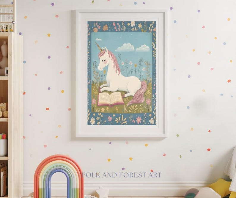 May include: A framed art print featuring a white unicorn with a pink mane and tail, reading a book in a field of flowers. The artwork is set against a blue sky with clouds, framed in a white border. The text "FOLK AND FOREST ART" is at the bottom.
