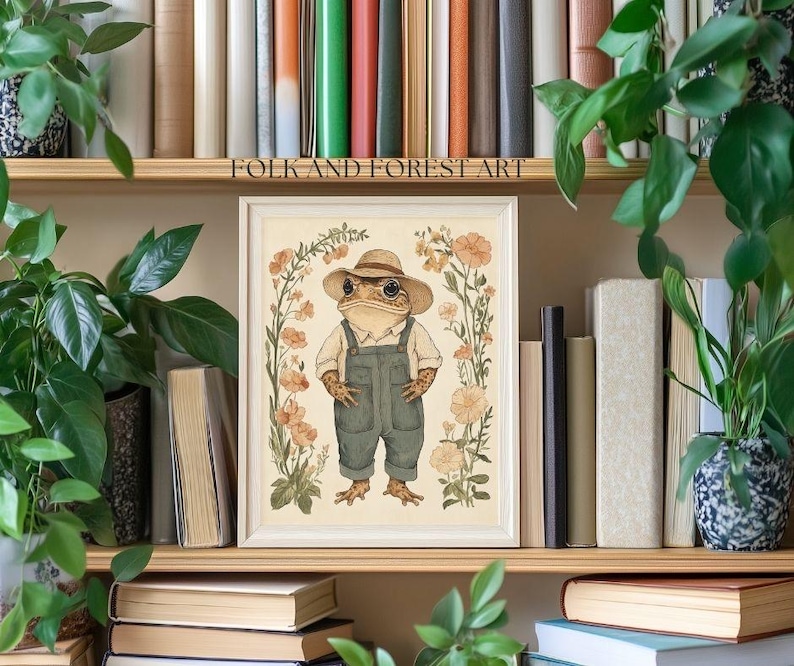 May include: A framed illustration of a frog wearing a hat and overalls, standing in a field of flowers. The illustration is in a watercolor style and has a vintage aesthetic. The text "FOLK AND FOREST ART" is at the top of the frame.