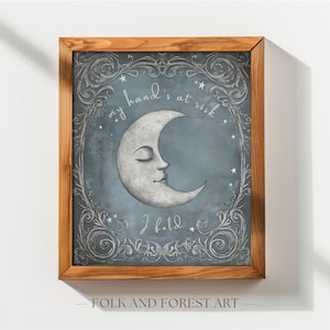 May include: A framed art print featuring a crescent moon with a face, surrounded by ornate scrollwork and stars on a blue background. The text "my hand's at risk, I hold" is written around the moon. The frame is made of wood.