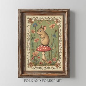 Peut inclure: Une impression d'art encadrée représentant une souris sur un champignon rouge à pois blancs, entourée de fleurs. L'œuvre d'art a une esthétique vintage avec un fond vert et un cadre en bois marron. Le texte "FOLK AND FOREST ART" est en bas.