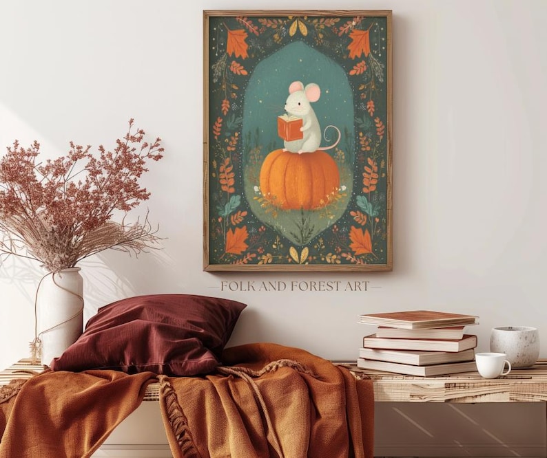 Op de afbeelding: Een ingelijste kunstprint toont een witte muis die een boek leest op een oranje pompoen, tegen een achtergrond van herfstbladeren. Het kunstwerk bevat de tekst "FOLK AND FOREST ART" en is ingelijst in een houten lijst.