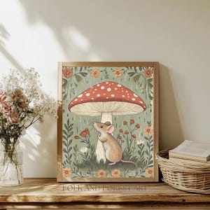 Puede incluir: Una impresi&oacute;n art&iacute;stica enmarcada con una ilustraci&oacute;n caprichosa de un rat&oacute;n resguard&aacute;ndose bajo una gran seta roja y blanca con lunares. La obra de arte tiene una paleta de colores suaves con elementos florales y bot&aacute;nicos. El texto "FOLK AND FOREST ART" est&aacute; en la parte inferior.