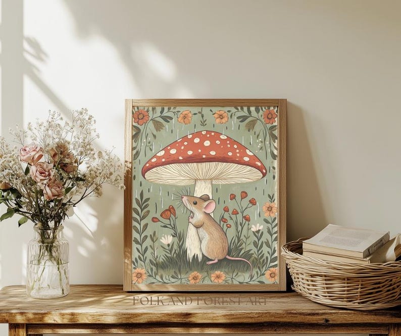 Puede incluir: Una impresi&oacute;n art&iacute;stica enmarcada con una ilustraci&oacute;n caprichosa de un rat&oacute;n resguard&aacute;ndose bajo una gran seta roja y blanca con lunares. La obra de arte tiene una paleta de colores suaves con elementos florales y bot&aacute;nicos. El texto "FOLK AND FOREST ART" est&aacute; en la parte inferior.
