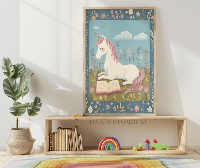 May include: A framed art print featuring a white unicorn with a pink mane and tail, reading a book in a field of flowers. The artwork has a blue background with clouds and a decorative floral border. The text "FOLK AND FOREST ART" is visible.