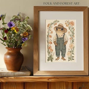 May include: A framed illustration of a frog wearing a straw hat and overalls standing in a field of flowers. The illustration is titled "Folk and Forest Art".