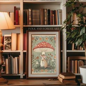 Puede incluir: L&aacute;mina art&iacute;stica enmarcada con una ilustraci&oacute;n caprichosa de un rat&oacute;n bajo una seta roja y blanca con lunares. La obra de arte, etiquetada como "FOLK AND FOREST ART", est&aacute; ambientada sobre un fondo de flores y follaje, con un marco de madera.