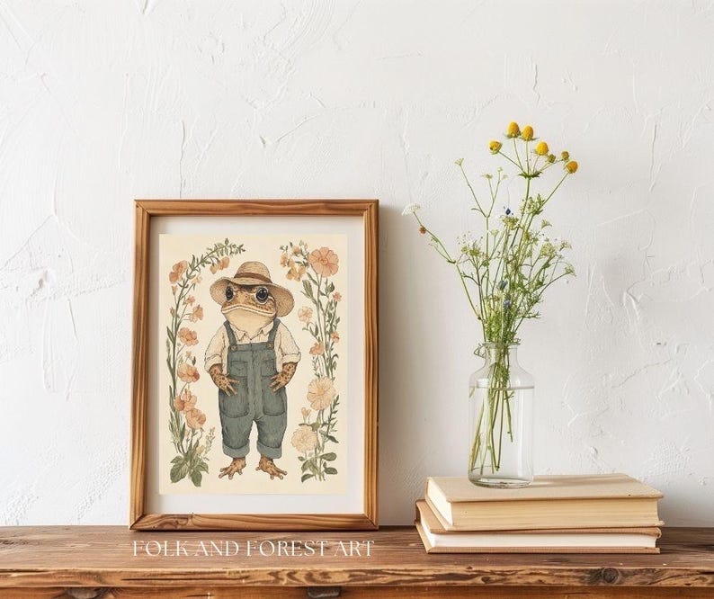 May include: A watercolor illustration of a frog wearing a straw hat and overalls standing in a field of flowers. The illustration is framed in a brown wood frame and the text "FOLK AND FOREST ART" is printed below the frame.