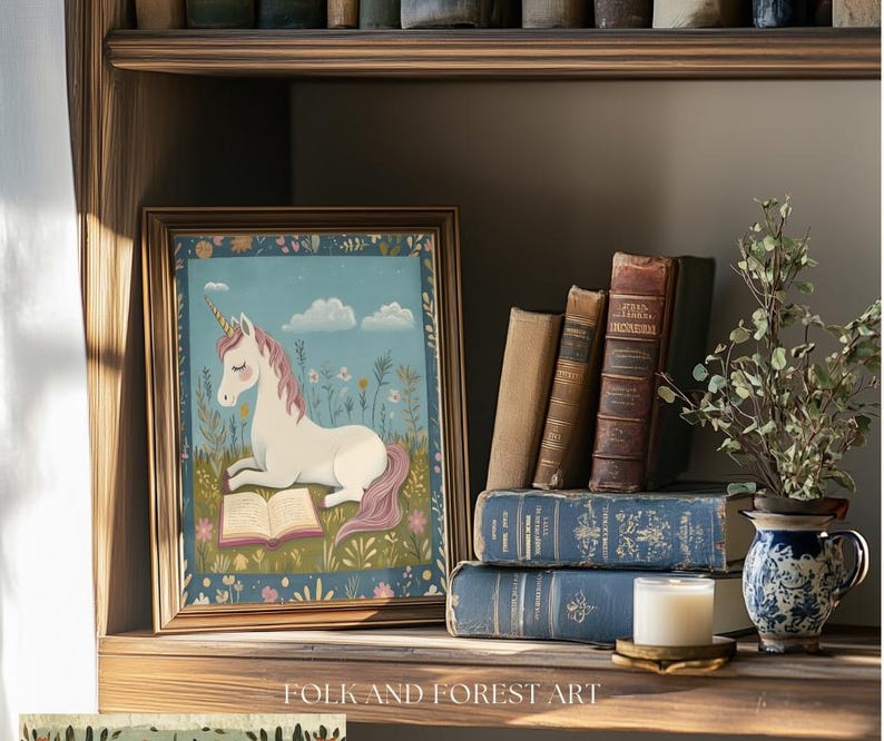 May include: A framed print of a unicorn reading a book, set on a wooden shelf with antique books and a small vase of greenery. The unicorn has a white body, pink mane and tail, and a golden horn. The print is surrounded by a gold frame.