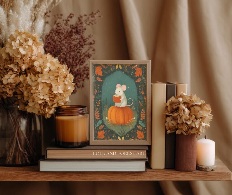 Op de afbeelding: Een ingelijste kunstdruk met een muis die een boek leest op een pompoen. De print staat op een houten plank met boeken, een kaars en droogbloemen. De tekst "FOLK AND FOREST ART" is zichtbaar. Herfsttinten.