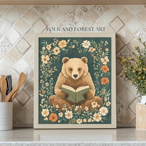A cozy folk art illustration featuring a brown bear sitting among wildflowers, holding an ornate green book. The green background complements the warm tones of the bear and florals. Perfect for book lovers, woodland nursery decor, and cottagecore.