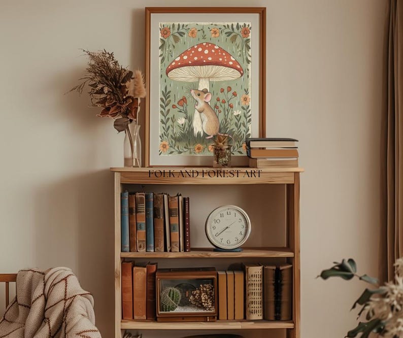 Puede incluir: Una impresi&oacute;n art&iacute;stica enmarcada que presenta una ilustraci&oacute;n de un rat&oacute;n bajo una seta roja y blanca. La obra de arte se encuentra sobre un fondo verde y floral. La impresi&oacute;n se exhibe en una estanter&iacute;a de madera con libros, un reloj y objetos decorativos.