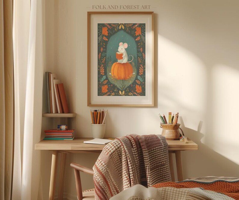 Op de afbeelding: Ingelijste kunstdruk met een witte muis die een boek leest op een oranje pompoen. De achtergrond is donkerblauwgroen met bloemen en bladeren. De lijst is lichtbruin. Een charmant kunstwerk.