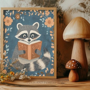 Puede incluir: Ilustración enmarcada de un mapache leyendo un libro, rodeado de elementos florales en tonos naranja y azul. La obra de arte está sobre un fondo texturizado, con una pieza decorativa de hongo de madera a la derecha. El texto "FOLK AND FOREST" está en la parte inferior.