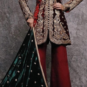 May include: A formal outfit comprising a burgundy velvet jacket with gold embroidery and wide-leg trousers. A dark green velvet shawl with gold detailing adds a touch of elegance. Suitable for special occasions, the outfit is a statement piece.