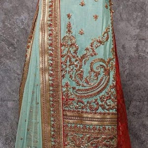 May include: A detailed embroidered outfit in seafoam green and red. The garment features gold threadwork, sequins, and a sheer dupatta. The design includes paisley and floral motifs, creating a luxurious and elegant look. The bottom is a vibrant red with a gold pattern.