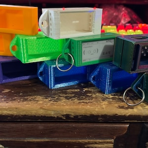 May include: A stack of colorful plastic cases with key rings. The cases are various shades of blue, green, orange, and white. Some of the cases have a small window.