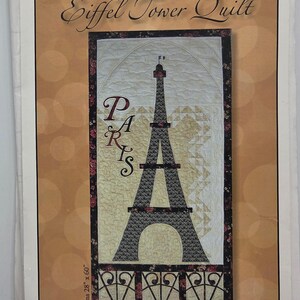 May include: A quilt pattern booklet titled Eiffel Tower Quilt featuring a vertical design of the Eiffel Tower in black and cream tones with the word PARIS written vertically in dark red. The quilt measures 28 inches by 60 inches as printed.