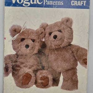 Könnte beinhalten: Vogue Patterns Schnittmuster mit zwei braunen Teddybären. Die Musternummer ist 621. Die Bären haben dunkelbraune Augen und Nasen. Ein Bär hat eine weiße Schleife. Entworfen von Linda Carr.