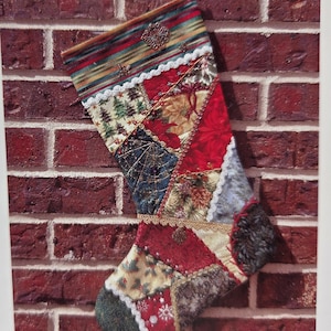 May include: A Christmas stocking constructed from a patchwork of various fabrics including red, green, and gold patterns. The stocking features decorative lace trim, metallic stitching, and small embellishments along the seams of the fabric pieces.